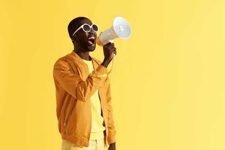 Man in yellow with yellow background shouting into megaphone