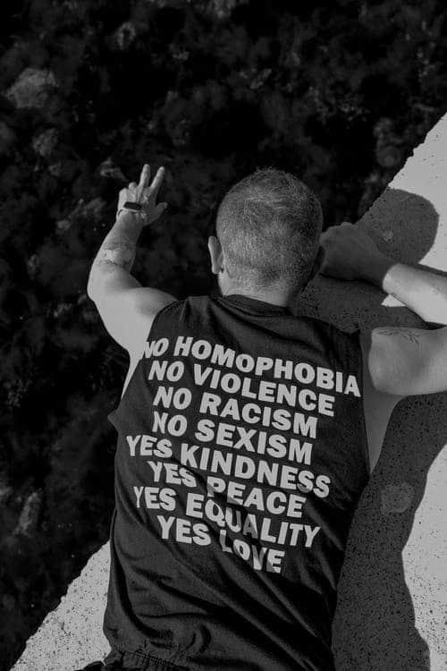 The back of a man wearing a sleeveless shirt that says no to homophobia, violence, racism, and sexism and promotes peace, love, and equality.