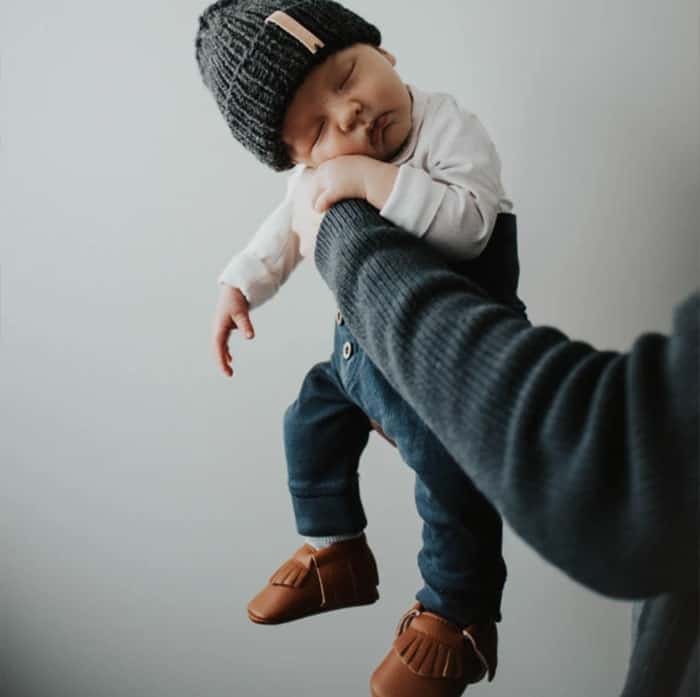 Sleeping baby in beanie held in air by parents arm