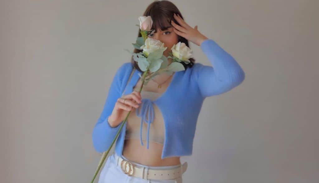 Barbara Doce in sexy blue cardigan holding white roses to her face