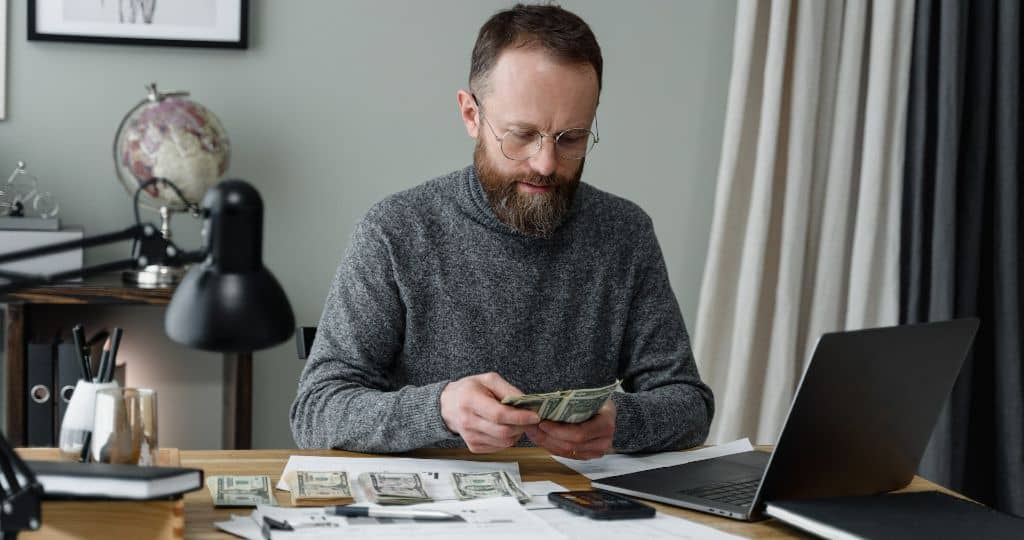 Bearded man in his office counting US banknotes to pay his influencers
