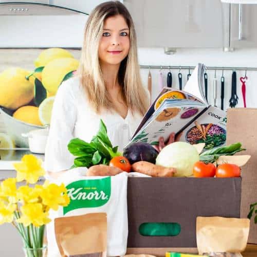 Bianca Zapatka |  Reading a recipe book with bags of veg on the side