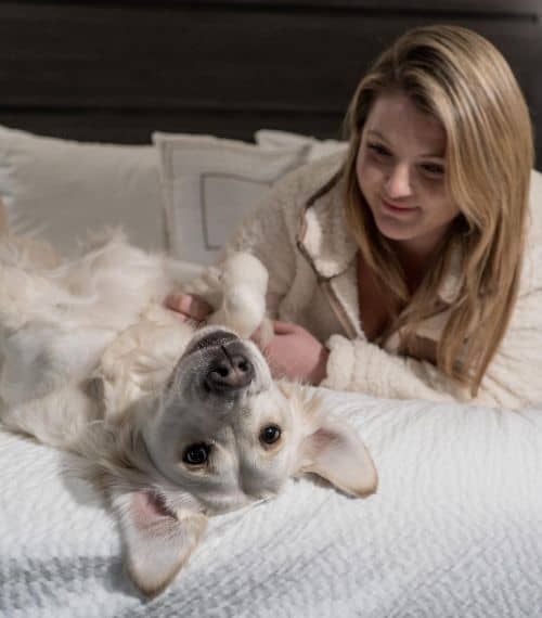 Brittany Brown and her dog Rosie all in white lying on the bed