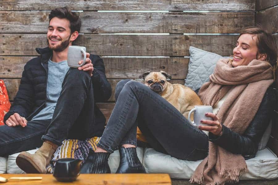 Man and woman in cabin drinking coffee with their pet dog