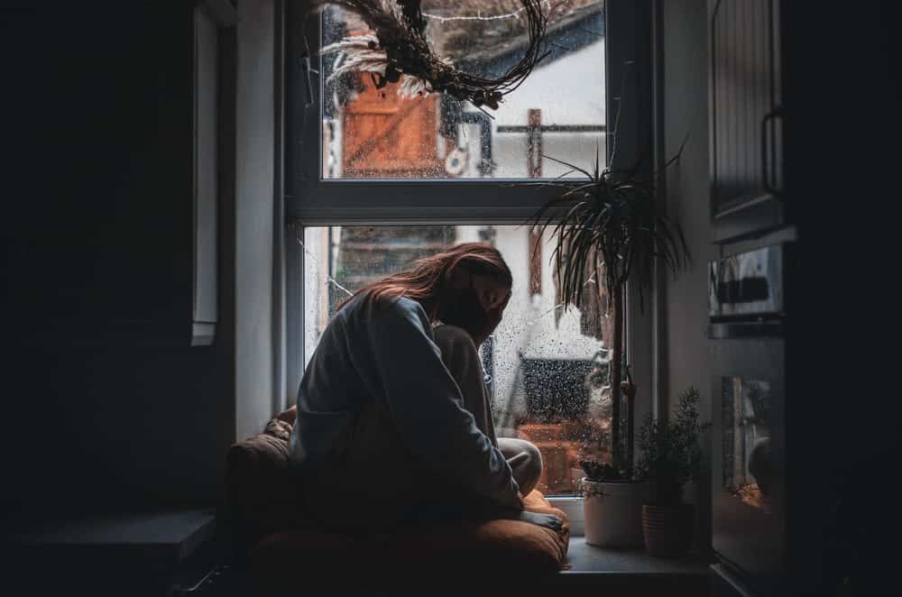 woman sat in the dark by window looking sad