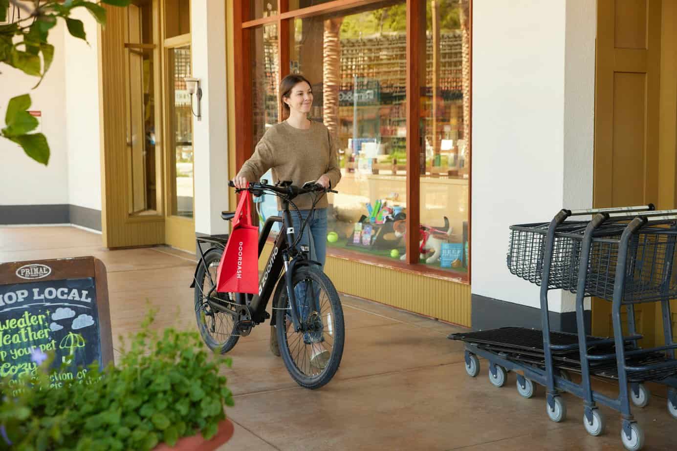 Doordash rider smiling while walking her Zoomo bike alongside a local shop