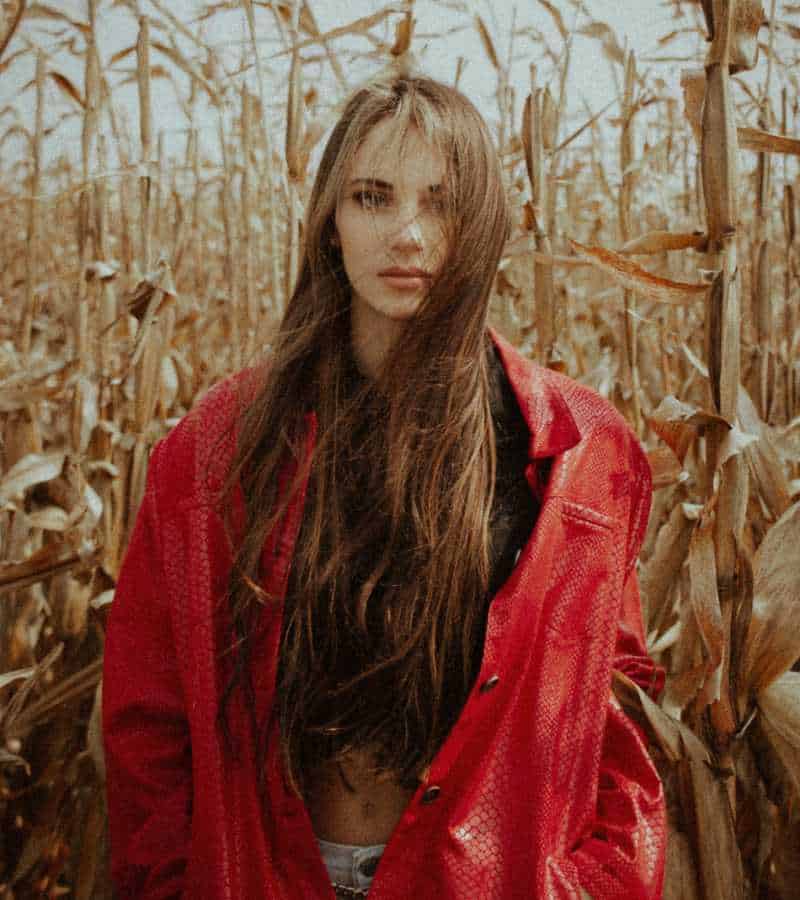 Long-haired fashion influencer in red jacket posing in the middle of a corn field