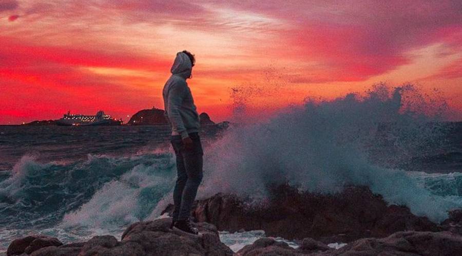 Florent Quilici standing on rocks splashed by waves during sunset