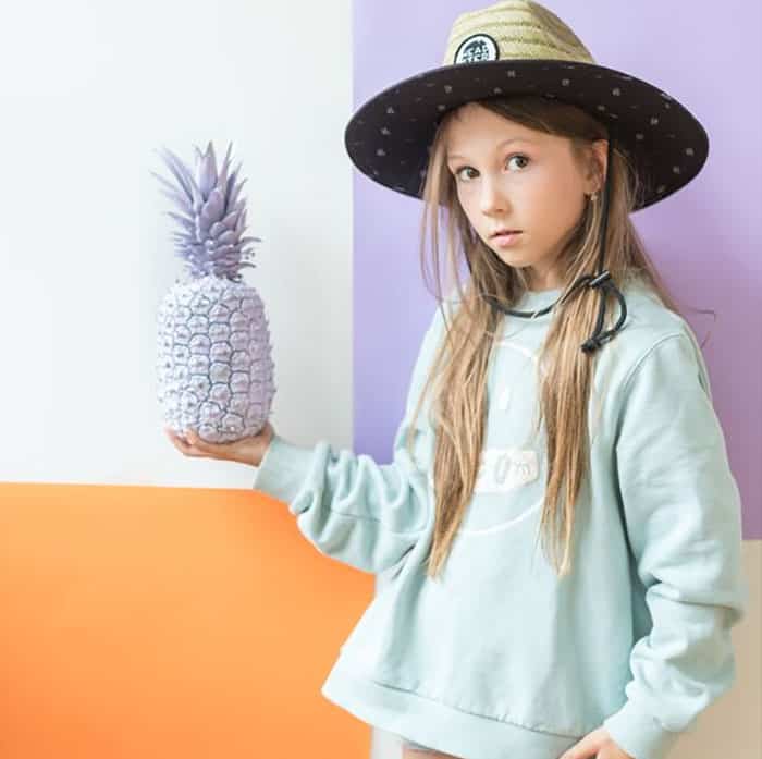 Girl in Headster hat holding a purple pineapple | Kids Clothing Brands