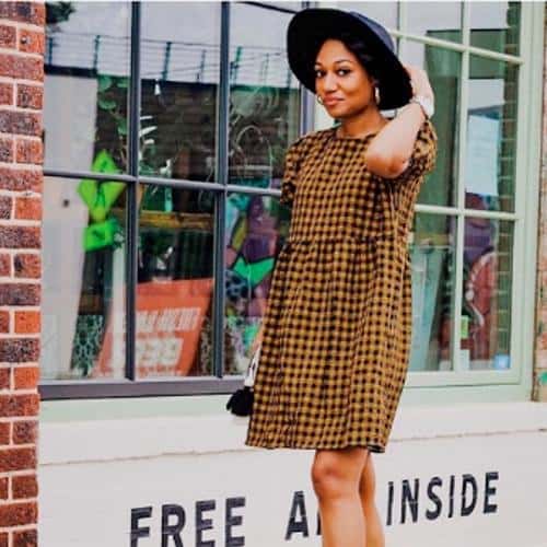 Jasmine Jones in dress and hat walking by shop window