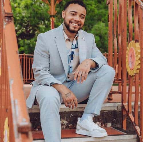 Kenny Ethan Jones suited up sitting on steps | Advocate of Body Positivity