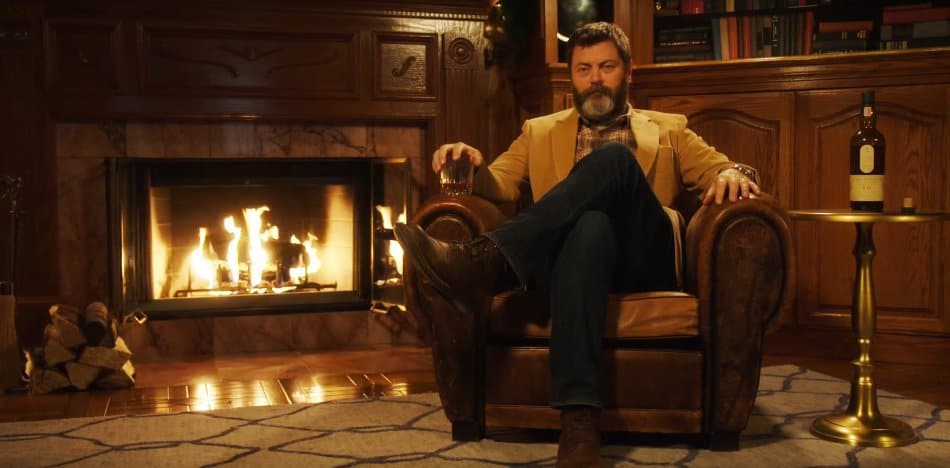 Nick Offerman sat on couch by fireplace with whiskey in hand
