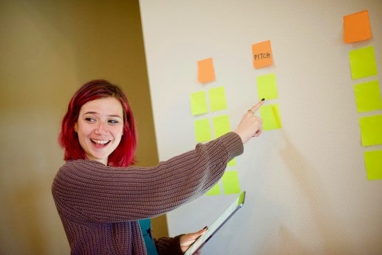 Read head woman smiling and pointing at board with sticky notes