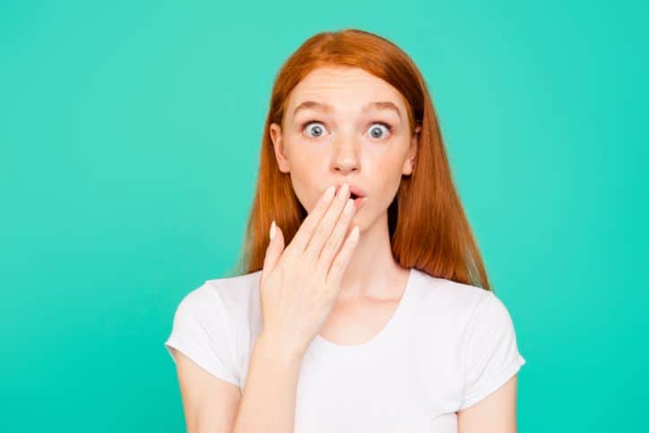 Girl in white top with blue background with fingers to her mouth