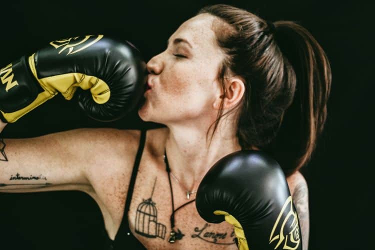 Woman boxer with tattoos kissing her black and yellow boxing glove