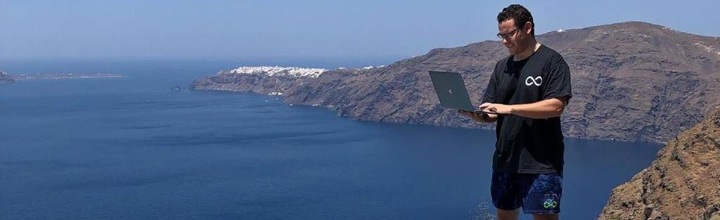 Timothy Sykes using his MacBook on top of a climb overlooking the ocean