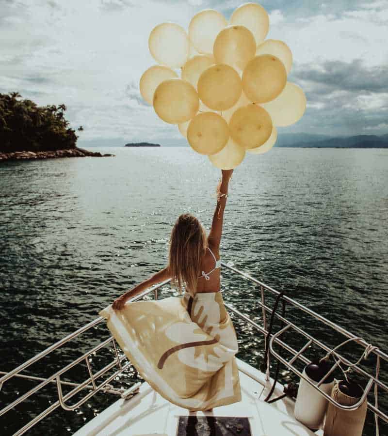 Fashion influencer on bow of yacht while hanging onto balloons